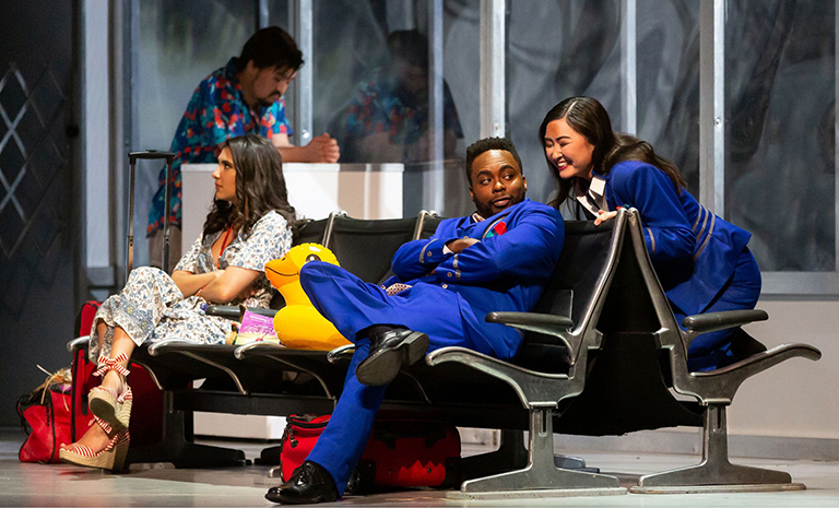 Several passengers and crew members wait out a storm in an airport terminal lounge in a scene from the Dallas Opera production of Flight.